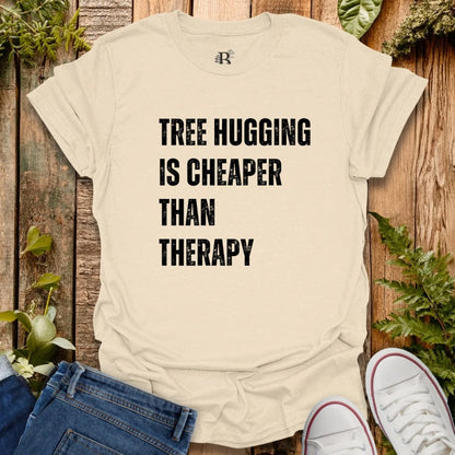 Beige t-shirt with 'Tree Hugging is Cheaper Than Therapy' text on a wooden background with plants.