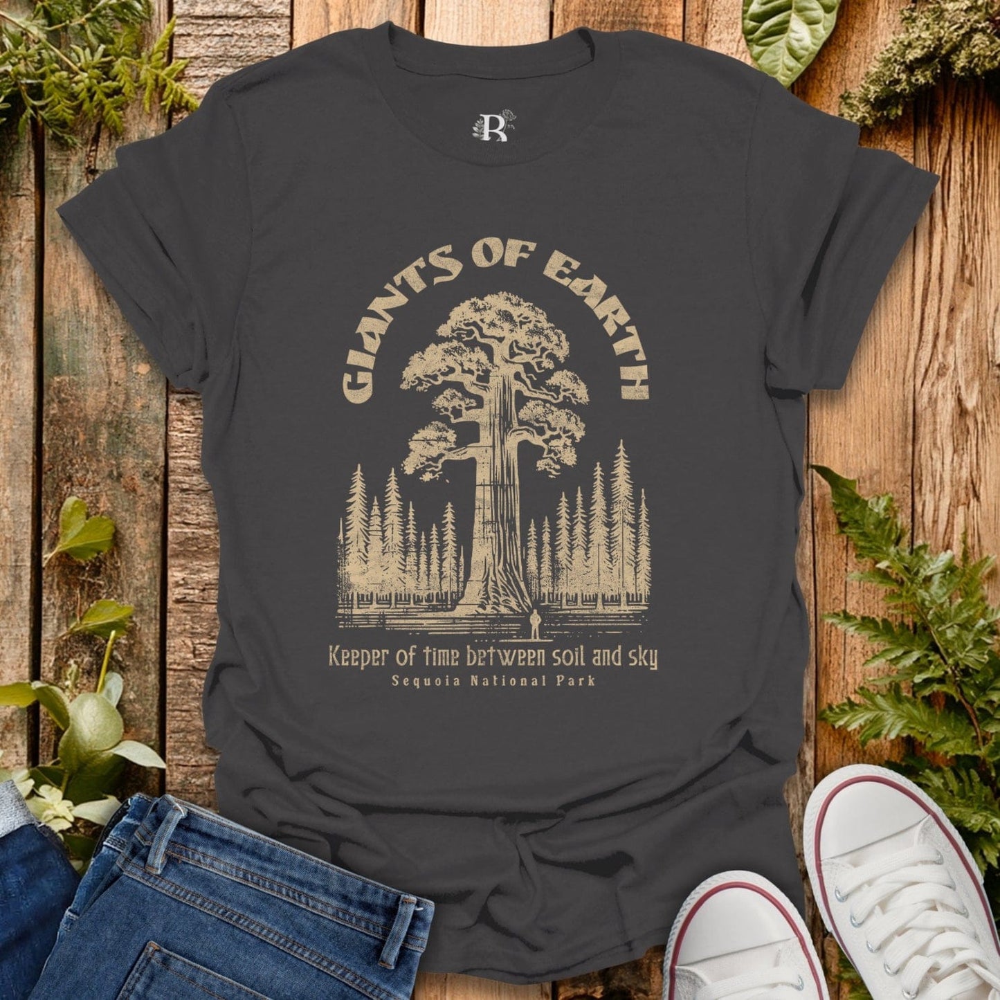 Dark gray t-shirt with 'Giants of Earth' graphic design on a wooden surface with plants.