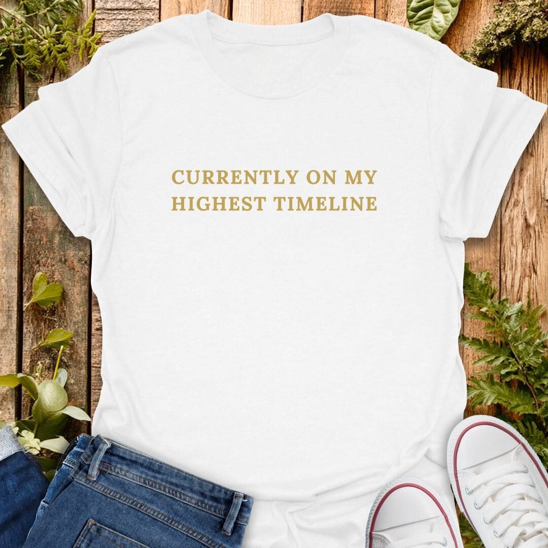 White t-shirt with 'Currently on my highest timeline' text on a wooden surface with plants, jeans and sneakers.